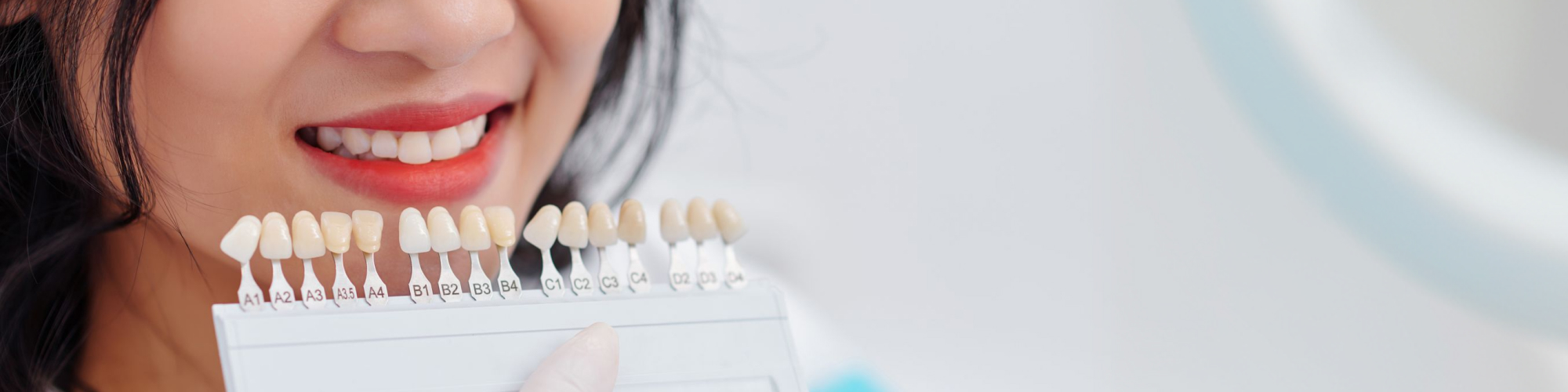 Gloved hand holding tooth shade-matching tool against woman's smile.
